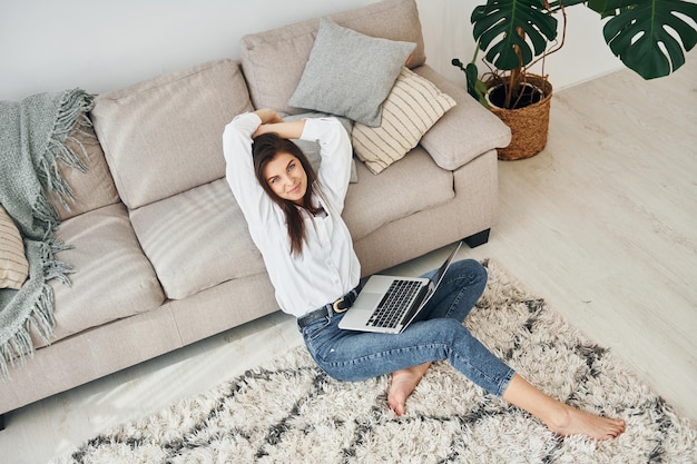 Mit Laptop Schöne junge Frau in Jeans und weißem Hemd ist zu Hause