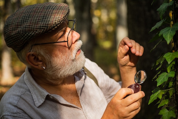 Mit Lupe untersuchen. Vergrößerung und Untersuchung. Zurück zur Natur. Alter Mensch im Wald, der die Natur erforscht. Forschung für den Naturschutz. Baumblätter mit Lupe untersuchen.