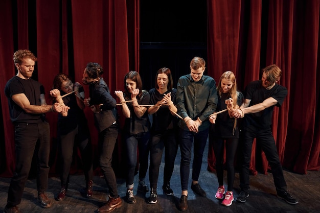 Mit Seil in Händen Gruppe von Schauspielern in dunkler Kleidung bei der Probe im Theater