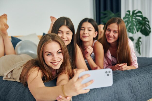 Mit Smartphone aufs Bett legen Gruppe glücklicher Frauen, die auf einer Junggesellenparty sind