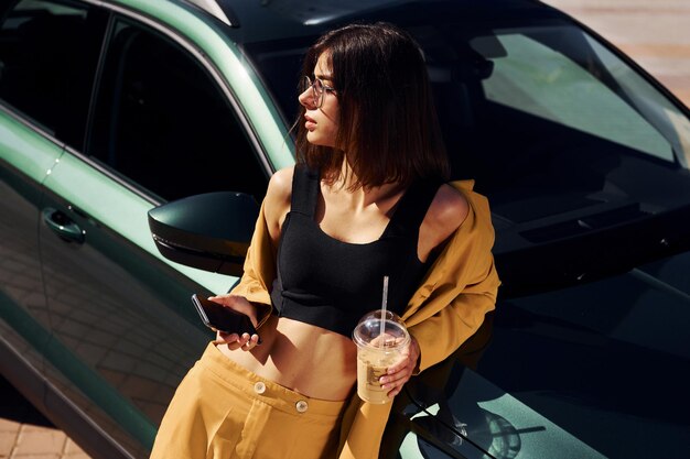 Mit Smartphone Junge modische Frau in burgunderfarbenem Mantel tagsüber mit ihrem Auto