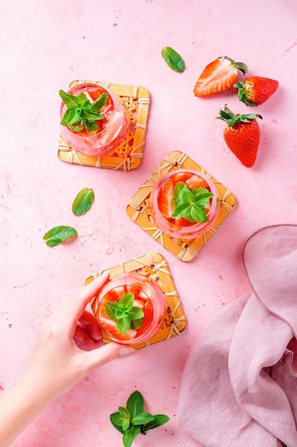 Mit Sommerminze und Erdbeeren angereichertes Wasser auf rosafarbener Tischplatte, flach, Ansicht von oben Sommerlich fruchtig erfrischendes Cocktail-Stillleben, Nahaufnahme