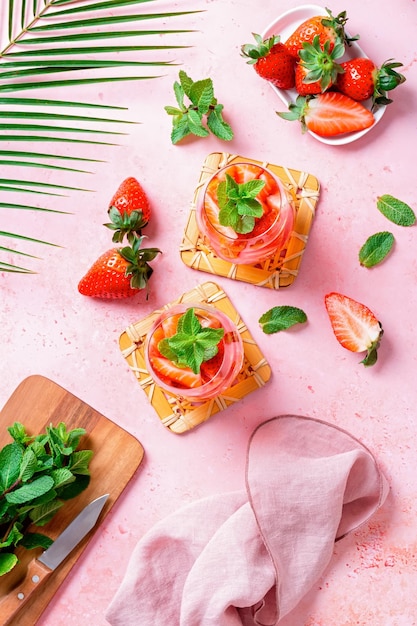 Mit Sommerminze und Erdbeeren angereichertes Wasser auf rosafarbener Tischplatte, flach, Ansicht von oben Sommerlich fruchtig erfrischendes Cocktail-Stillleben, Nahaufnahme