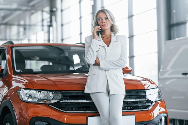 Mit Telefon Frau in formeller Kleidung ist drinnen im Autosalon