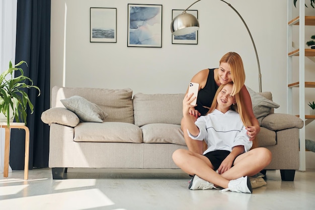 Foto mit telefon in den händen auf dem boden teenagerin mit ihrer mutter ist tagsüber zu hause