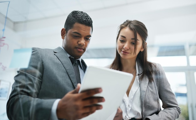 Mit tragbarer Technologie die Zahlen auf dem Laufenden halten Aufnahme eines jungen Geschäftsmanns und einer Geschäftsfrau, die ein digitales Tablet in einem modernen Büro verwenden