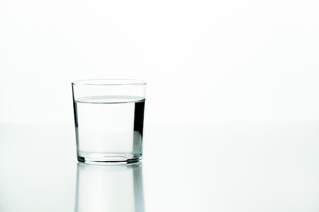 Mit Wasser gefüllter Glasbecher auf weißem Hintergrund mit minimalistischem Konzept und viel Platz zum Kopieren
