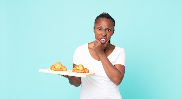 Mit weit geöffnetem Mund und weit geöffneten Augen und einer Hand am Kinn und hält ein Croissant-Tablett