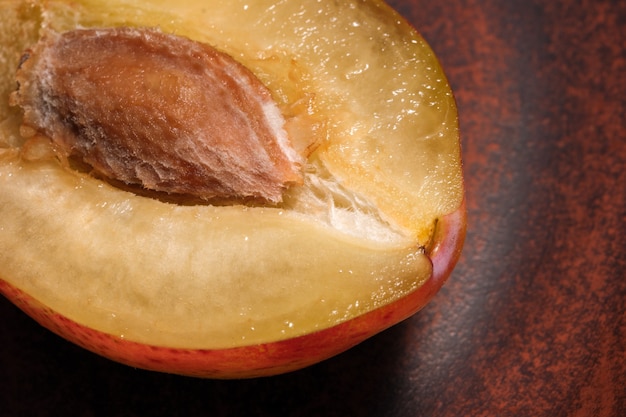 La mitad de ciruela dulce con piedra sobre placa de arcilla marrón fotografía macro de cerca