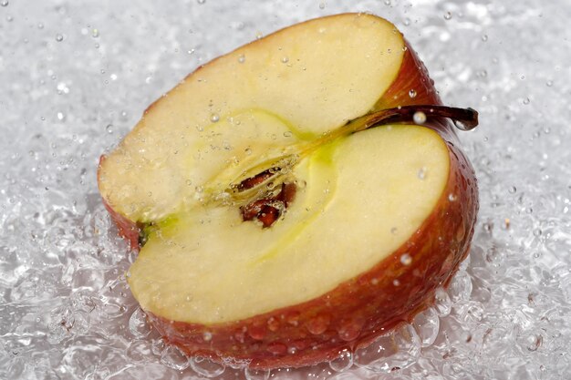 La mitad de una manzana dulce madura roja en un plato blanco se vierte con agua de una ducha desinfectante fotografía macro de cerca de frutas