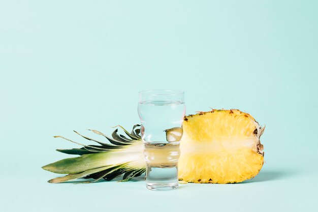 Foto la mitad de la piña con un vaso de agua.