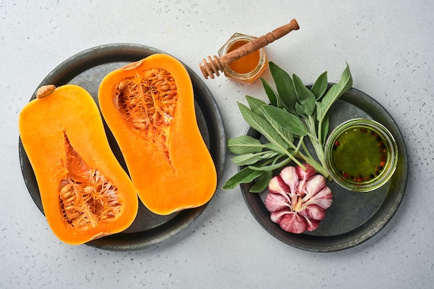 Mitades de calabaza orgánica cruda con hojas de salvia, ajo pimiento multicolor, miel, sal y pimienta sobre un fondo blanco de pizarra, piedra u hormigón. Fondo de alimentos. Vista superior con espacio de copia.