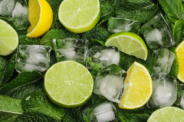 Foto mitades y gajos de limas y limones con cubitos de hielo sobre un fondo de menta fresca