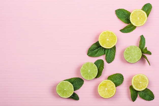 Foto mitades de limones y limas, menta sobre fondo de madera rosa, espacio de copia