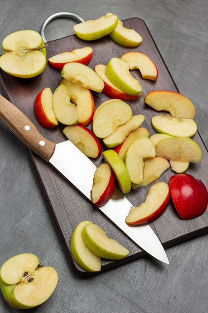 Foto mitades de una manzana verde rodajas de manzanas verdes y rojas y un cuchillo de cocina en la tabla de cortar