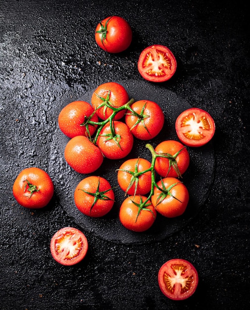 Mitades y tomates enteros en una rama en un tablero de piedra