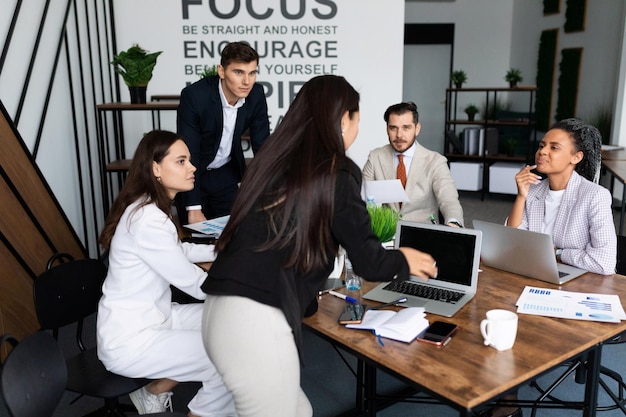 Mitarbeiter des Unternehmens diskutieren während einer Besprechung im Büro an einem großen Desktop mit Laptops und