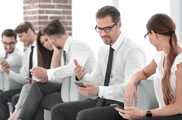 Mitarbeiter des Unternehmens sitzen mit ihren Smartphones in der Bürolobby