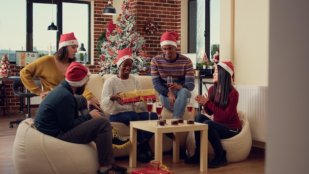 Mitarbeiter, die weihnachtsfeier im büro mit weihnachtsbaum und festlichen ornamenten beschenken. Geschenke austauschen und Überraschungen machen, um die Winterferienzeit bei einem Arbeitsereignis zu feiern.