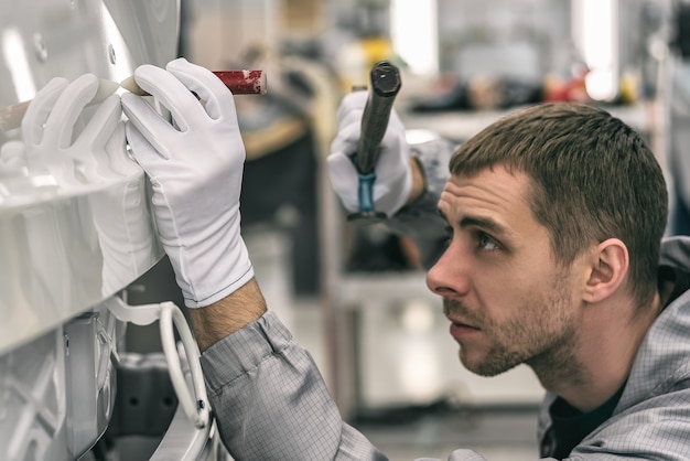 Mitarbeiter einer Autofabrik behebt kleine Metallfehler mit einem speziellen Handwerkzeug