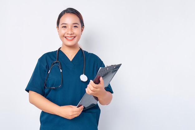 Mitarbeiter im Gesundheitswesen lächelnd junge asiatische Frau Krankenschwester tragen blaue Uniform mit einem Stethoskop hält Zwischenablage isoliert auf weißem Hintergrund Healthcare Medizin-Konzept