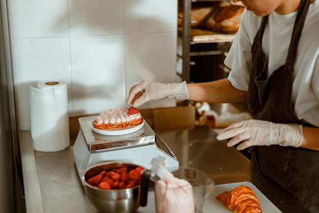 Mitarbeiter legt in handwerksbäckerei frische erdbeeren auf croissant mit sahne