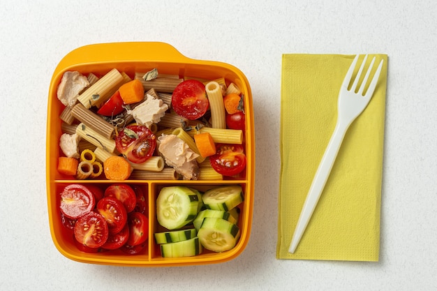 Mittagessen am Arbeitsplatz gesunde Pasta mit Thunfisch, Kirschtomaten, Karotten, Gurke in der Brotdose auf dem Arbeitstisch. Hauptnahrungsmittel für Bürokonzept