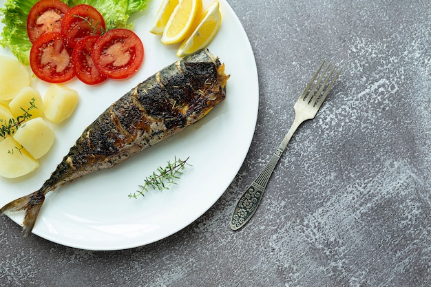 Mittagessen. Gebratene Makrele auf einem weißen Teller mit Kartoffeln und Salat, Draufsicht