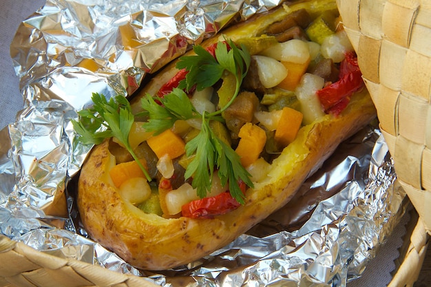 Mittagessen im Freien für Vegetarier – Kartoffeln mit Gemüse und Käse in einer Aluminiumfolie gebacken. Der Teller ist im Korb aus geflochtenem Birkenholz versteckt