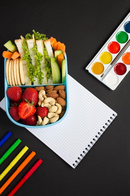 Mittagessen in der Schule in der blauen Box und Schulbriefpapier auf schwarzem Hintergrund Draufsicht Standort vertikal