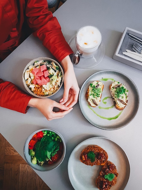 Mittagessen in einem Café, Lifestyle-Foto, Bruschettes, Schüsseln und Kaffee, Draufsicht auf den Tisch und weibliche Hände