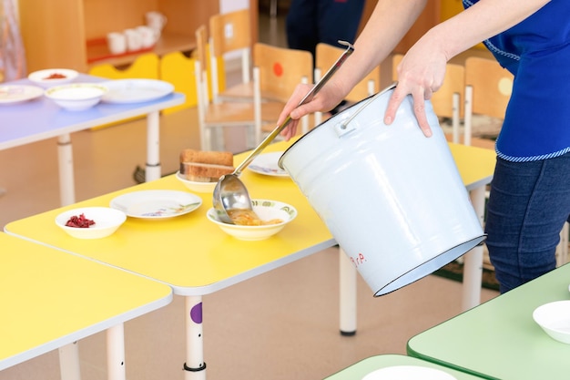 Mittagessen in einem Kindergarten in Russland Die Lehrerin stellt Suppe auf einen Teller