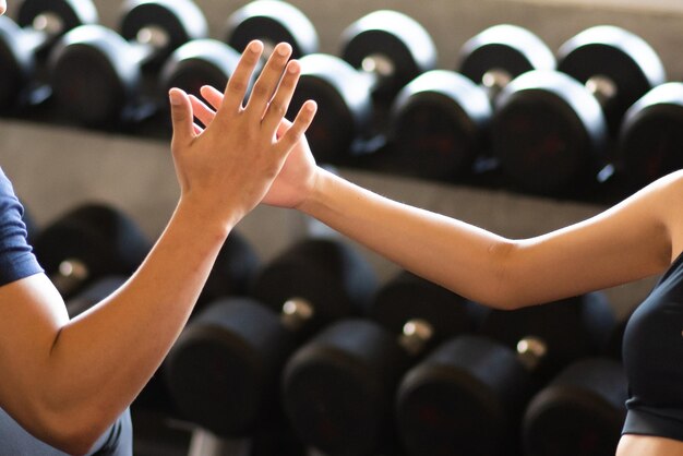 Mittelabschnitt einer Frau, die dem Ausbilder im Fitnessstudio High-Five gibt