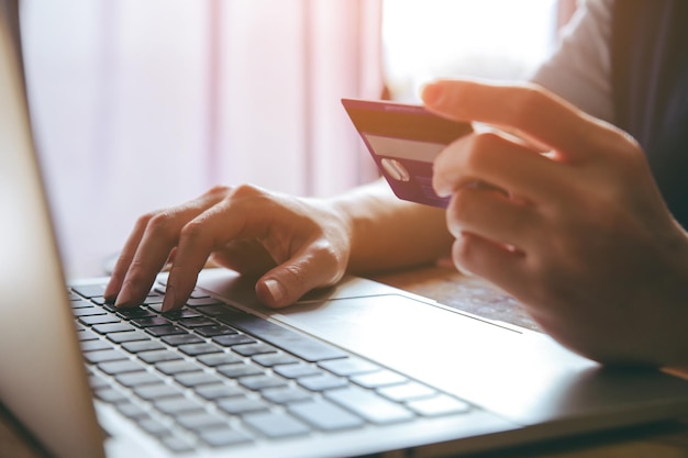 Foto mittelabschnitt einer frau, die eine kreditkarte hält, während sie einen laptop für online-shopping benutzt