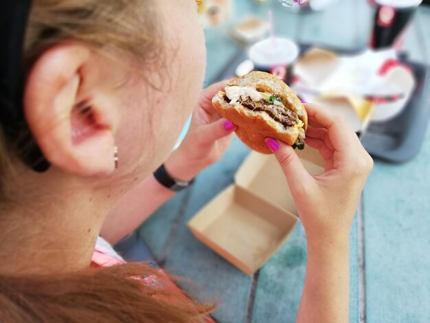 Foto mittelabschnitt einer frau, die einen burger am tisch isst