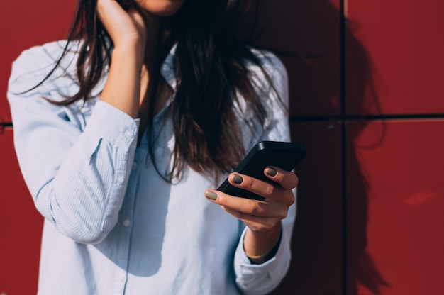 Mittelabschnitt einer Frau, die gegen die Wand steht und ein Handy benutzt