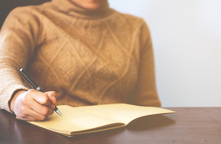 Foto mittelabschnitt einer frau, die gegen einen weißen hintergrund sitzt und auf ein buch schreibt