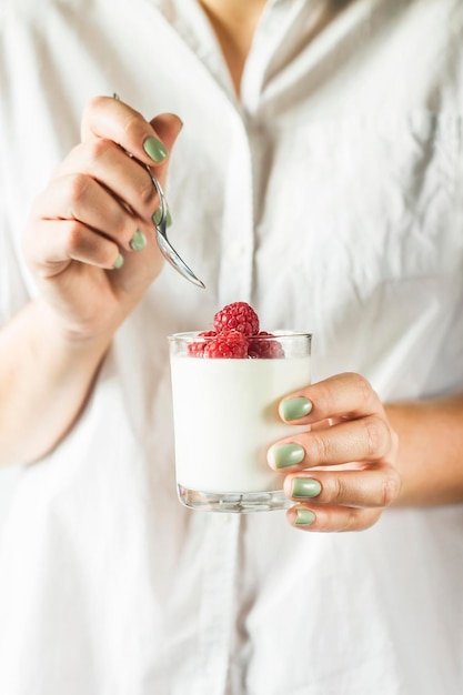 Foto mittelabschnitt einer frau, die joghurt und himbeeren in einem trinkglas hält