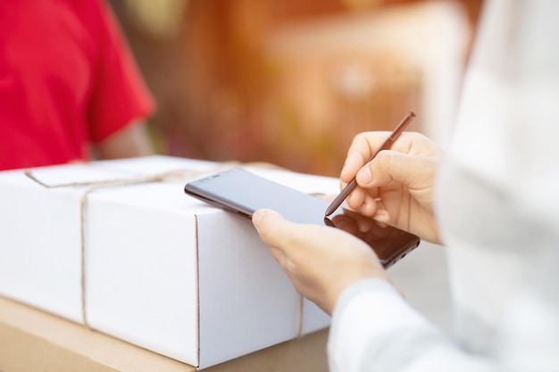 Mittelabschnitt einer Frau, die über ein Handy unterschreibt, während sie ein Paket von einem Lieferanten erhält