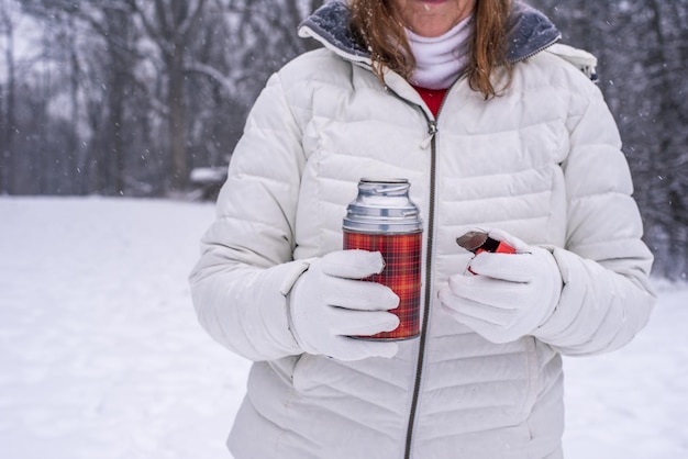 Mittelabschnitt einer Frau mit einer Flasche, die im Schnee steht