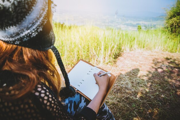 Foto mittelabschnitt einer frau sitzt und schreibt in einem buch auf dem feld