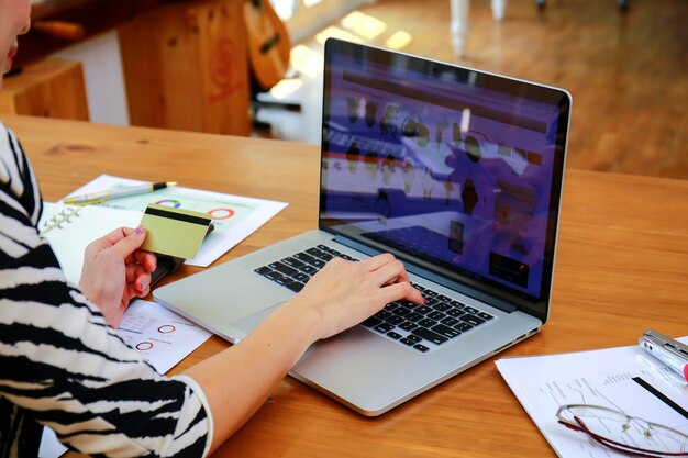 Foto mittelabschnitt einer geschäftsfrau, die eine kreditkarte hält, während sie einen laptop auf dem tisch benutzt