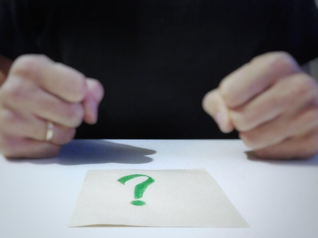 Foto mittelabschnitt einer person, die am fragezeichen auf einem papier auf dem tisch steht