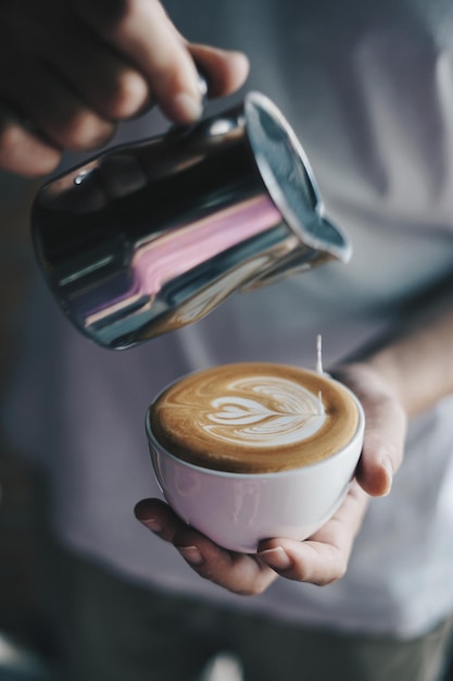 Mittelabschnitt einer Person, die Milch in Cappuccino gießt