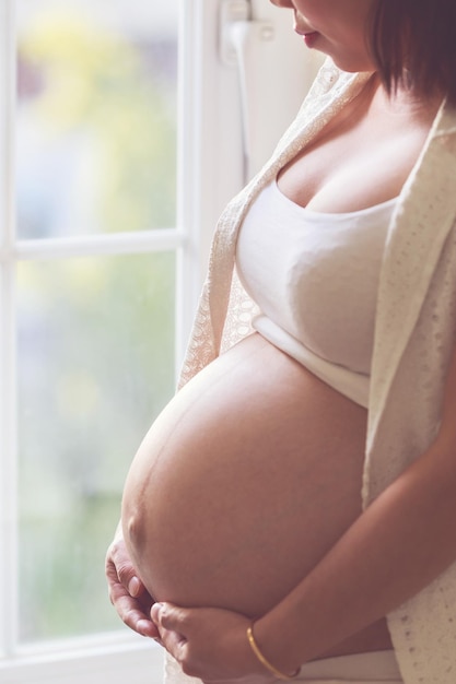 Mittelabschnitt einer schwangeren Frau, die am Fenster steht