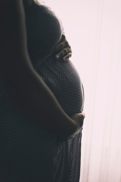 Mittelabschnitt einer schwangeren Frau, die am Vorhang steht