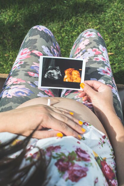 Foto mittelabschnitt einer schwangeren frau, die auf einem stuhl sitzt und ein ultraschallbild hält