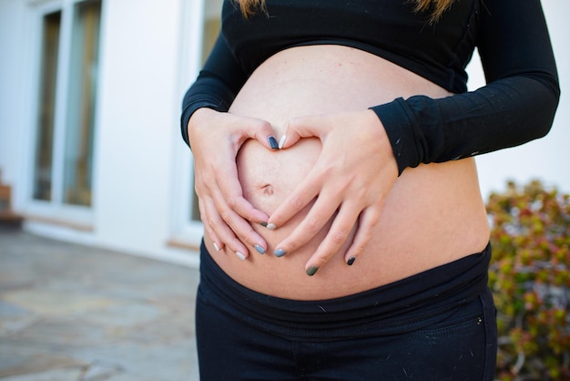 Mittelabschnitt einer schwangeren Frau, die auf ihrem Bauch eine Herzform bildet