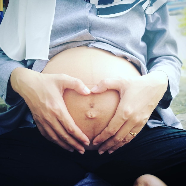 Mittelabschnitt einer schwangeren Frau, die auf ihrem Bauch eine Herzform bildet