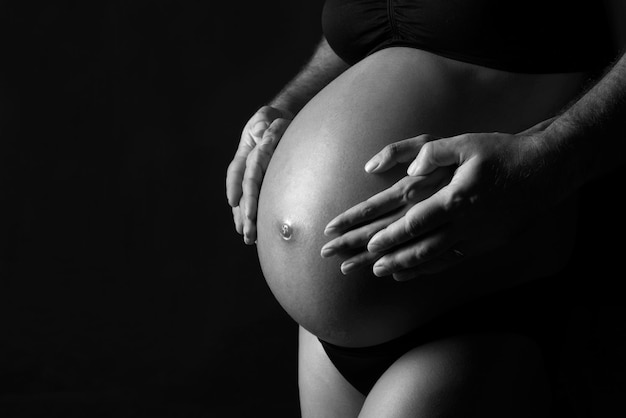 Mittelabschnitt einer schwangeren Frau, die ihren Bauch gegen schwarzen Hintergrund berührt